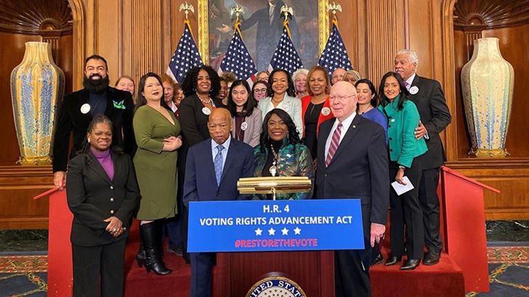 People in suits behind sign with text ‘Voting Rights Advancement Act’