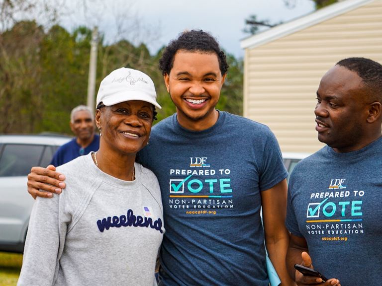 Picture of three Black people smiling with voting shirts. 