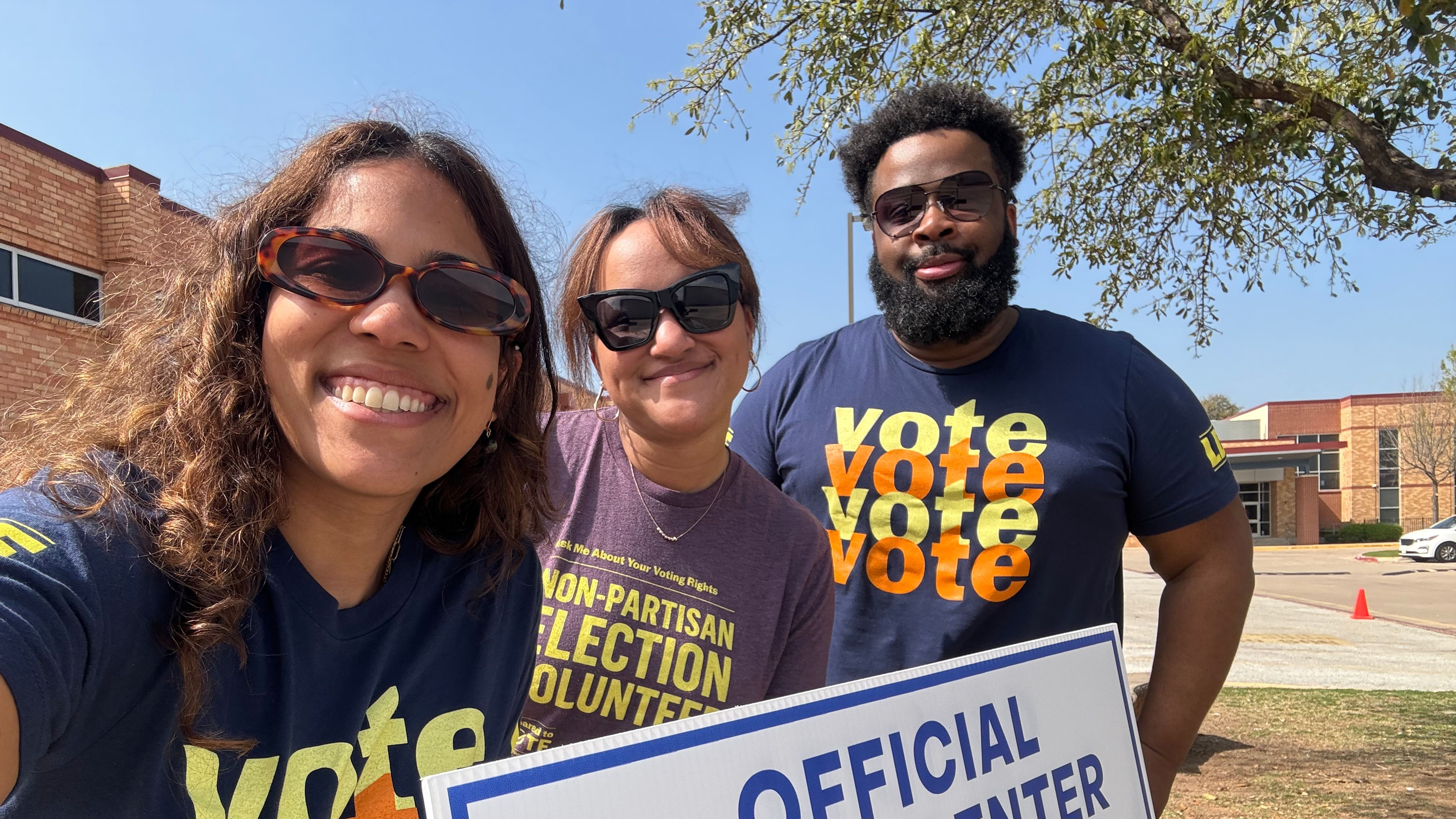 Three nonpartisan election volunteers outside a poll site on a sunny day wearing sunglasses