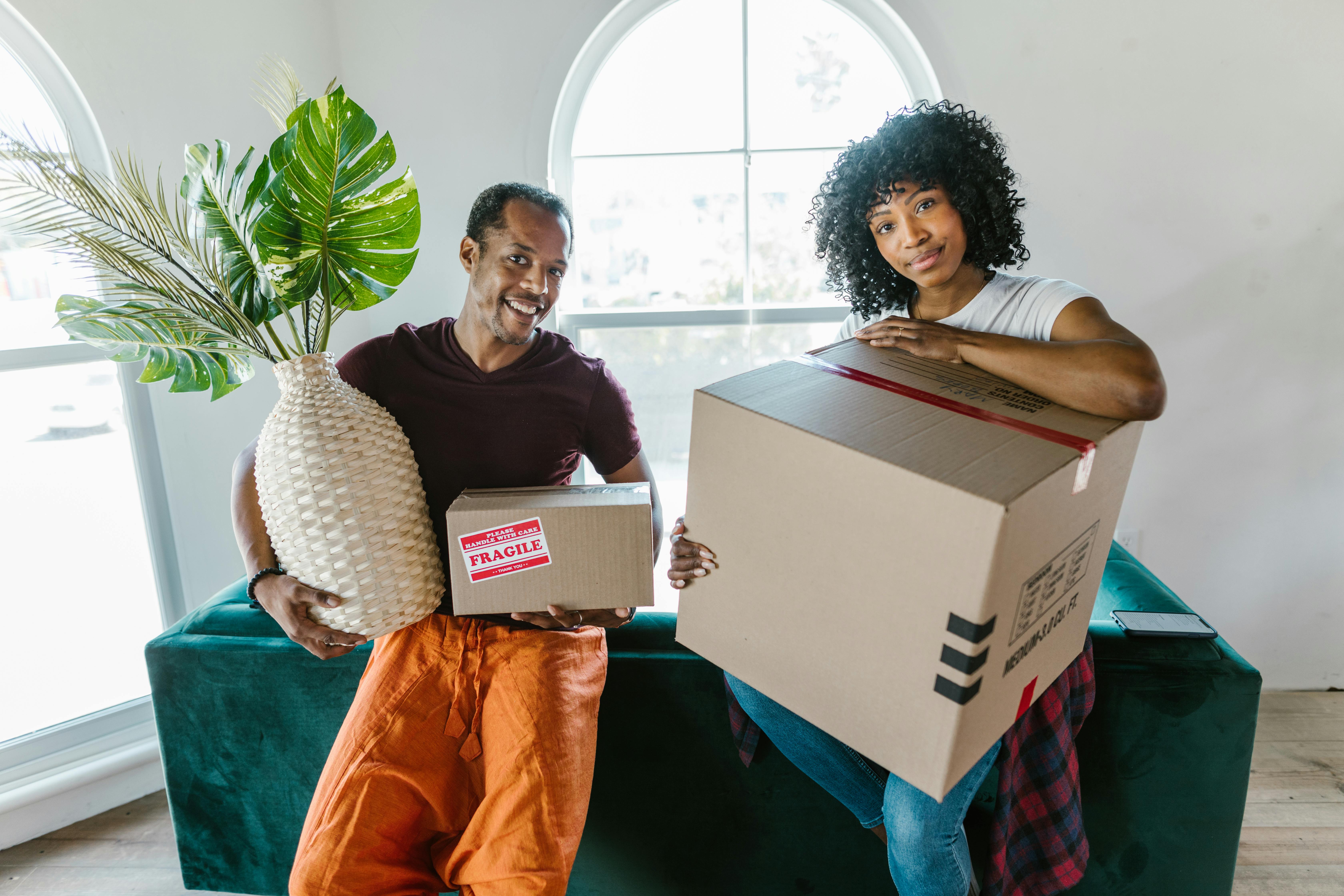 Two people in new house holding moving boxes and decor