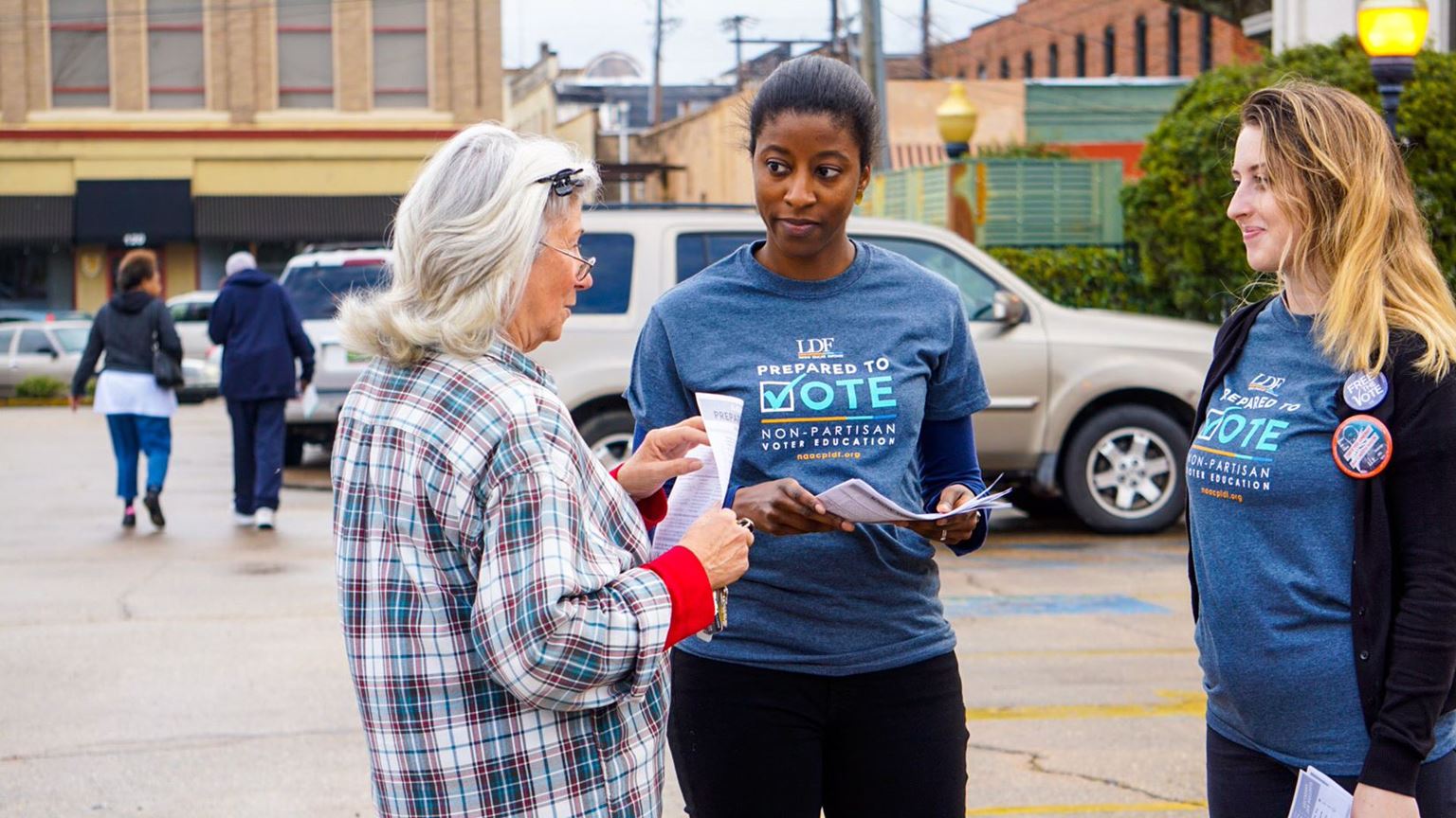 Three women discussing voting issues in a parking lot.