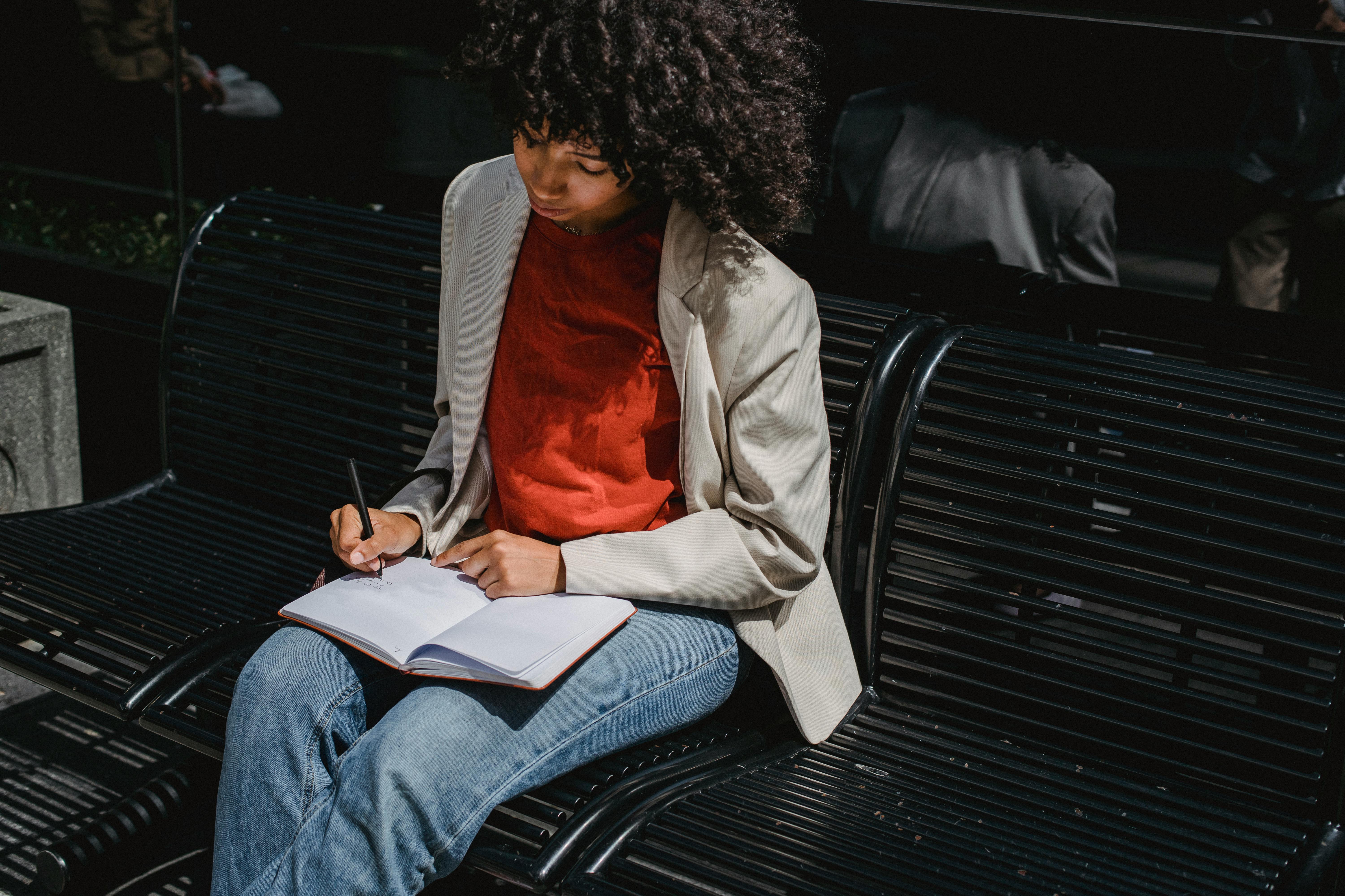 Student writing in a notebook on a park bench